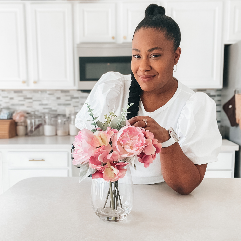 Tiffany Harrison, Motherhood and Lifestyle Blogger from Tiffanydoesitall.com, the working moms guide to balancing family and business. posing in kitchen with pink flowers
